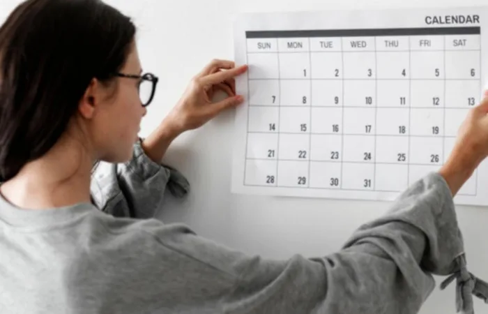 A woman hanging a calendar on a wall