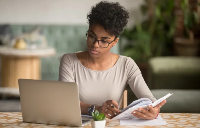 Woman looking at her laptop while holding her notebook