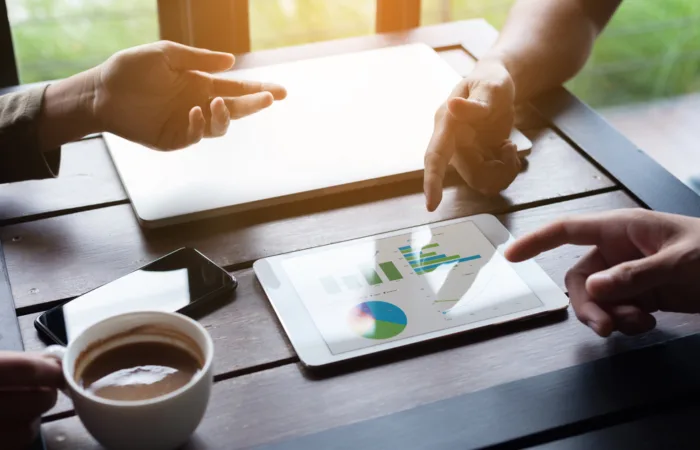 Hands of several people discussing a graph on a tablet
